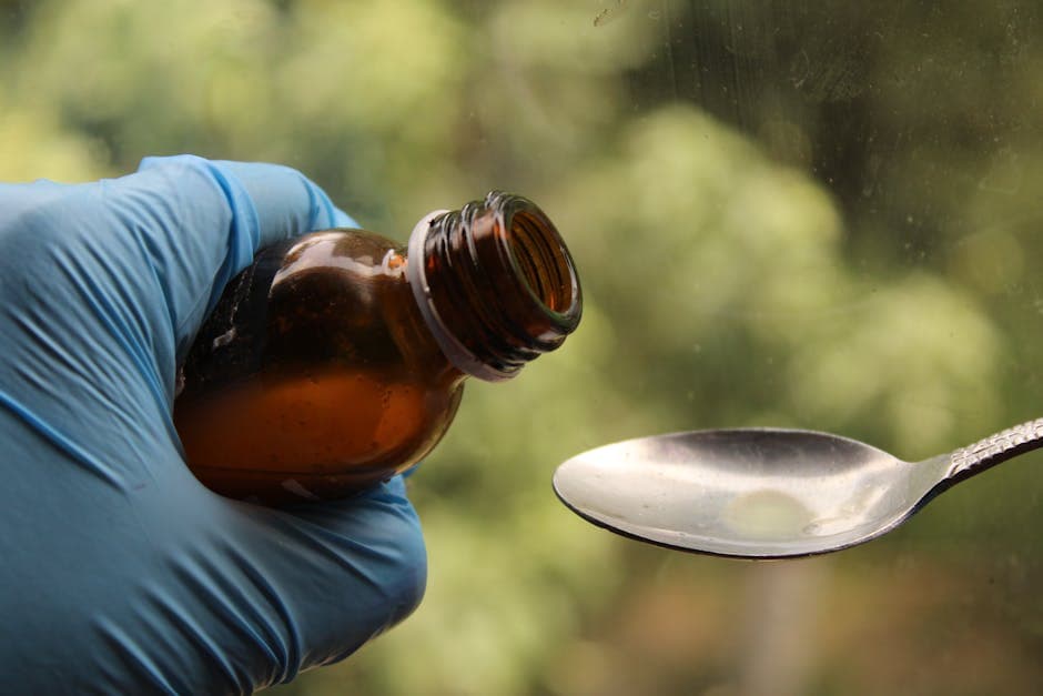 Close-up of a gloved hand pouring medicine into a spoon, blurred background.