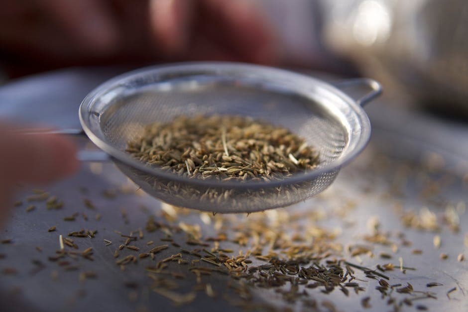 Selective focus on herbs being strained through a sieve, capturing culinary detail.