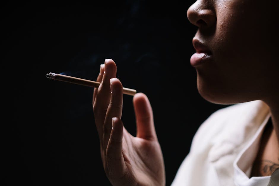 A close-up of a person holding and smoking a cigarette against a dark background.