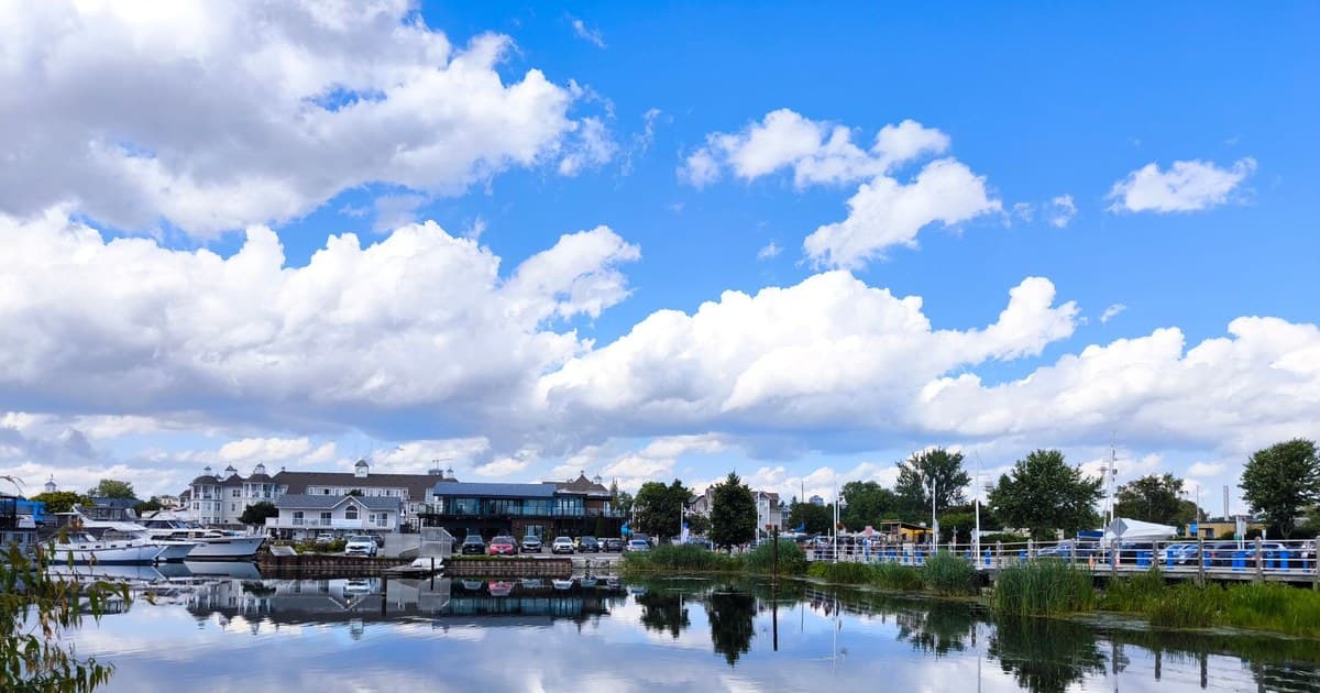 Reflective water scene with boats and clouds under a bright blue sky in a tranquil waterfront town.