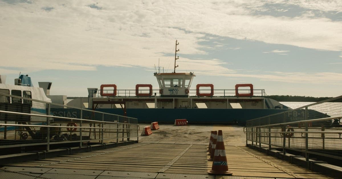 A ferry docked at a harbor under a cloudy sky with visible traffic cones.