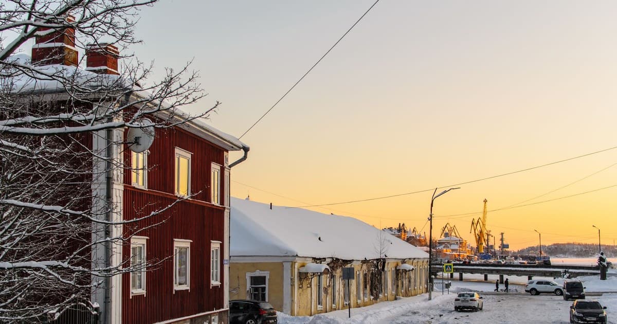 Scenic view of a snowy harbor town at sunset, featuring colorful buildings and a serene winter landscape.